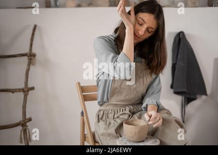 femme caucasienne fatiguée avec mal de tête au travail dans un atelier de céramique. Création de poteries faites à la main. Lady sculpte un bol fait à la main. Banque D'Images