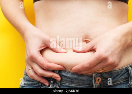 Les mains de la femme comprime la graisse sur son ventre sur un fond jaune Banque D'Images