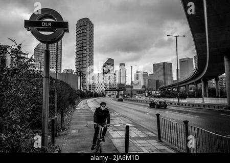 Le paysage urbain de l'est de Londres, un cycliste passe tout en marchant le long de West India Dock Road vers l'île des chiens. Banque D'Images