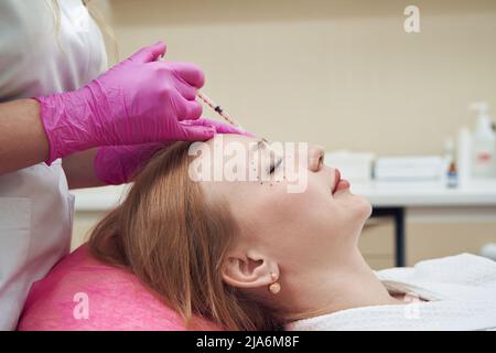 Femme gaie recevant des injections de beauté dans le beau visage dans la clinique Banque D'Images