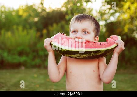 joyeux sourire enfant garçon mangeant de la pastèque à l'extérieur dans l'arrière-cour Banque D'Images