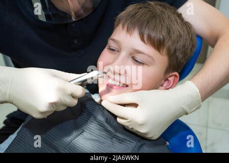 Le portrait d’un enfant et les mains d’un enfant dentiste avec des pinces dentaires, un gros plan. Banque D'Images