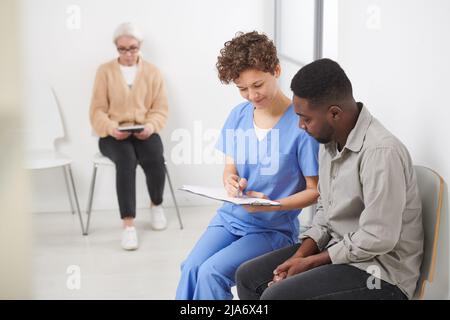 Une femme caucasienne médecin assise sur une chaise dans le couloir de l'hôpital montrant les résultats des tests sanguins à sa patiente afro-américaine Banque D'Images