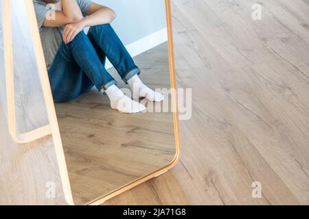Réflexion dans le miroir d'une femme triste assise sur un sol seul dans la pièce vide, désespoir et concept solitaire avec espace de copie Banque D'Images