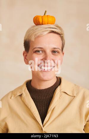 Portrait de fille de tomboy souriant avec des cheveux courts gardant la petite citrouille sur la tête contre fond beige, concept d'Halloween Banque D'Images