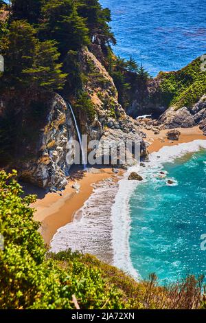 Cascade cachée sur une plage de sable avec vagues de l'océan colorées Banque D'Images