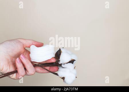 Mains d'une femme tenant des cotons-tiges et des fleurs de coton pour nettoyer la peau sur un fond beige Banque D'Images