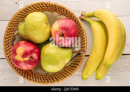 Deux poires biologiques juteuses, deux pommes rouges et un bouquet de bananes avec un plat en céramique sur une table en bois, vue rapprochée, vue de dessus. Banque D'Images