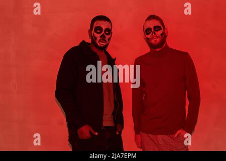 Portrait de jeunes hommes confiants avec maquillage zombie debout contre le mur dans la pièce sombre avec lumière rouge Banque D'Images