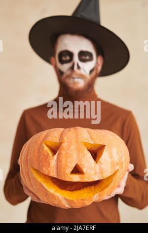 Homme barbu avec maquillage de crâne portant des sorcières chapeau tenant la citrouille sculptée à Halloween Banque D'Images