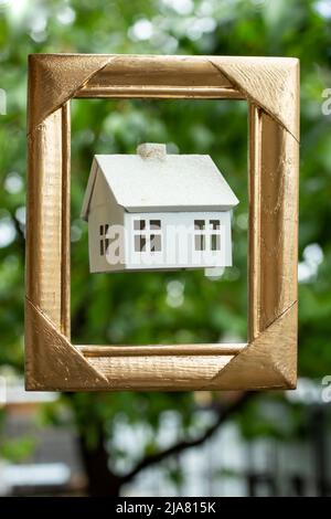 présentation d'une maison modèle blanche dans un cadre doré avec des arbres en arrière-plan. Banque D'Images