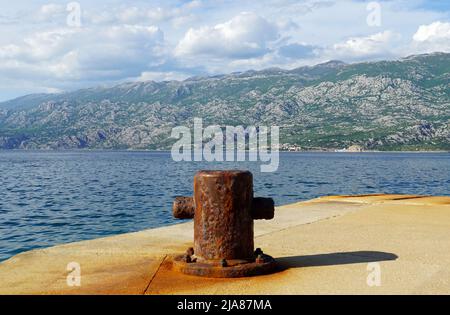 Vieil amarrage rouillé sur le quai de mer en face d'une haute montagne Banque D'Images