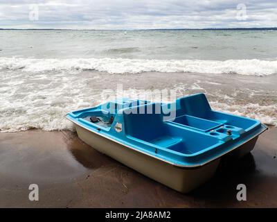 Un bateau à pédales vide se trouve sur la plage à marée montante, avec le plancher plein d'eau sous un ciel nuageux Banque D'Images