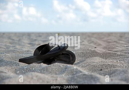 Une paire de tongs laissées dans le sable sur la plage sous un ciel bleu de nuages blancs bouffis Banque D'Images