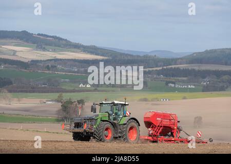Une vue vers la Suie sur un paysage agricole à Aberdeenshire, avec un tracteur vert Fendt et un semoir rouge semant de l'orge dans le champ le plus proche Banque D'Images