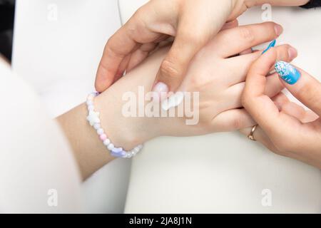 Un manucure applique de la crème pour les mains aux mains des femmes après une manucure de quincaillerie dans un salon de beauté. Coeur tiré sur la main, crème pour la main. Appliquer la crème sur y Banque D'Images