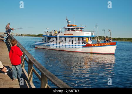 Un bateau de pêche affrété passe devant un jeune enfant et son père qui pêchent depuis un quai dans le parc national de Captree sur long Island Banque D'Images