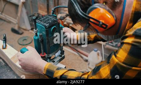 Menuiserie à l'intérieur - un menuisier polit les détails en bois du haut de l'atelier - un homme utilisant des casques de protection Banque D'Images