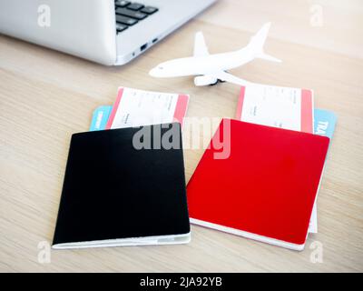 Noir et rouge, couleur différente de deux passeports avec couverture vierge avec deux billets d'avion près de l'ordinateur portable et jouet d'avion sur le bureau avec un bateau à soleil Banque D'Images