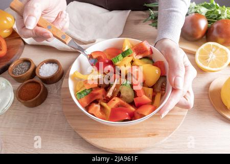 un grand bol de salade de légumes fraîchement préparée. la main de la jeune fille tient une fourchette avec des morceaux de laitue à essayer Banque D'Images