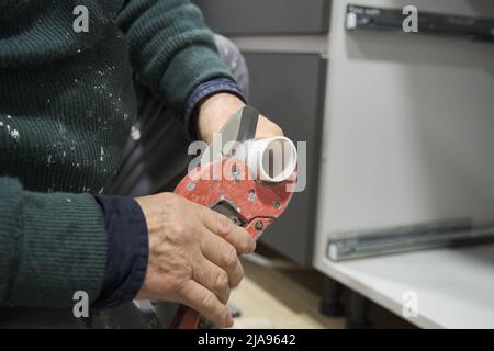 Plombier mûr coupant le tuyau pour installer le siphon d'évier dans la cuisine. Banque D'Images