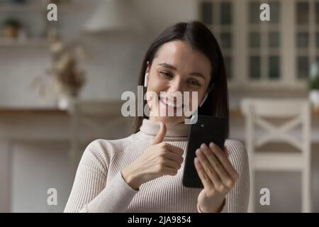 Bonne jeune femme millénaire utilisant des écouteurs sans fil et un téléphone portable Banque D'Images