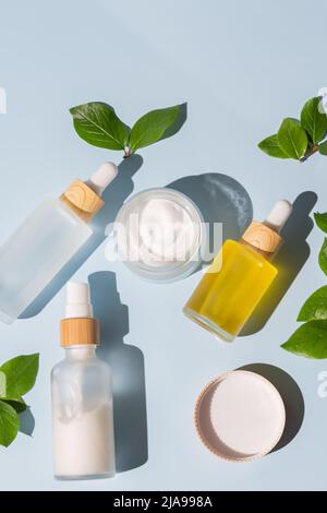 Pot de crème hydratante, sérum en bouteille de verre et toner avec feuilles vertes sur fond bleu. Flat lay, vue de dessus. Kit pour soins de la peau et du corps Beauty pro Banque D'Images