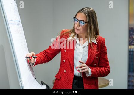 RIVNE, UKRAINE - 22 FÉVRIER 2022. Femme dans une veste rouge tenant une présentation d'affaires. Femme d'affaires attirante dans une veste rouge près du flich Banque D'Images