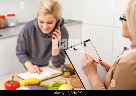 Une nutritionniste souriante conseille une jeune femme sur la nutrition et le régime appropriés. Le médecin montre un schéma de perte de poids sans un mauvais effet sur Banque D'Images