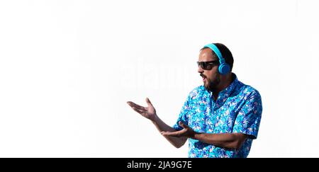 un jeune boxeur avec une barbe, des lunettes de soleil, une chemise hawaïenne et des écouteurs bleus fait un visage surpris montrant ce qui est à côté de lui avec les deux mains. Sur Banque D'Images