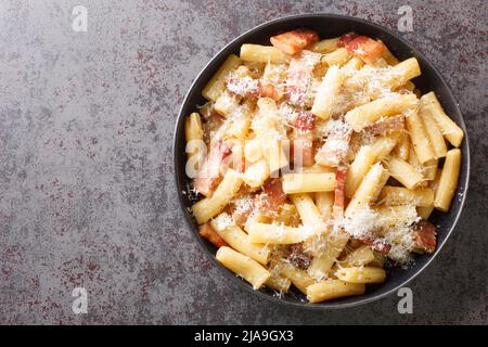 Pâtes italiennes alla grincia dans une assiette avec pecorino romano râpé et guanciale à proximité sur la table. Vue horizontale du dessus Banque D'Images