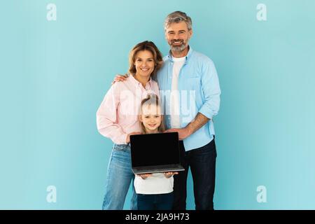 Famille de trois montrant l'écran vide de l'ordinateur portable sur fond bleu Banque D'Images