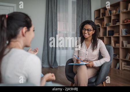 Jeune femme noire souriante médecin psychologue consultante femme européenne dans l'intérieur moderne de la clinique Banque D'Images