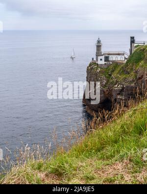 Côte rocheuse abrupte surcultivée avec de l'herbe verte, yacht solitaire en mer et phare de Santa Catalina (phare de Lequeitio) Cap El Cabo Antzoriz Banque D'Images