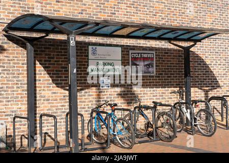 Un abri de vélo de conseil Basingstoke avec un porte-vélo et des vélos et une affiche d'avertissement "voleurs de vélo nous vous regardent" avec une paire d'yeux. ROYAUME-UNI Banque D'Images