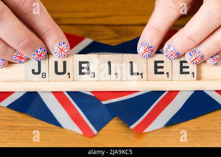 Doigts de femme avec ongles peints avec le drapeau britannique tenant des lettres scrabble qui sort Jubilé - le jubilé de platine de la Reine juin 2022 Banque D'Images