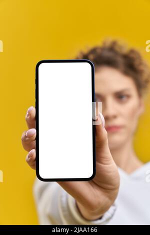 Grave fille floue montrant allumé à l'écran téléphone en studio. Vue rognée d'un smartphone de poche féminin avec écran blanc vierge, isolé sur fond orange, espace de copie. Concept de gadget. Banque D'Images