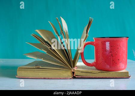 Livre ouvert, livre rigide vintage et vieille tasse de café sur fond de sarcelle. Éducation, lecture, concept de recherche. Banque D'Images