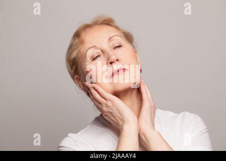 Belle femme âgée touchant son visage gros plan portrait Banque D'Images