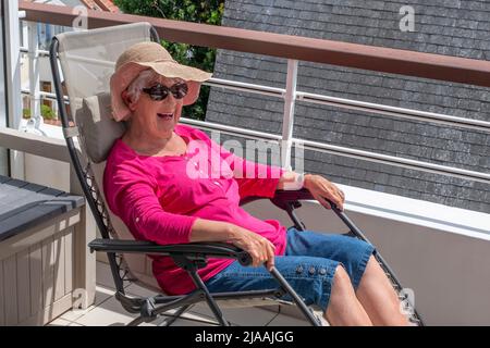 Une femme âgée souriante assise dans une chaise longue sur la terrasse d'un appartement Banque D'Images