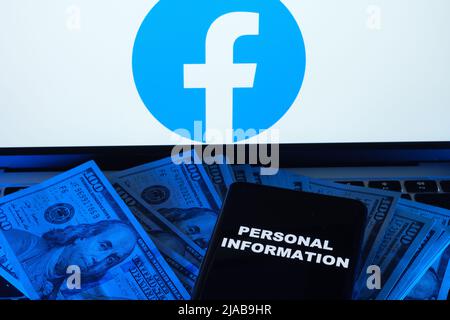 Mots INFORMATIONS PERSONNELLES vues sur le smartphone placé sur dollars et logo Facebook sur ordinateur portable flou derrière lui. Concept. Stafford, Royaume-Uni, mai Banque D'Images