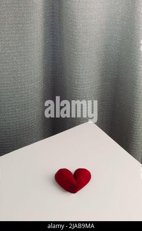 Deux pétales de rose rouge en forme de coeur sur une table blanche. Pose à plat. Fond de rideau en soie brillant gris. Composition de la Saint-Valentin ou de la fête des mères. Banque D'Images