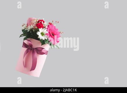 Boîte cadeau rose avec différentes fleurs colorées sur fond gris. Concept de la nature esthétique de la Saint-Valentin. Idée de carte du 8 mars. Banque D'Images