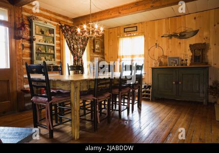 Table ancienne, chaises hautes à l'arrière et mobilier dans la salle à manger à l'intérieur de la vieille maison en bois de style cottage Canadiana datant de 1825. Banque D'Images