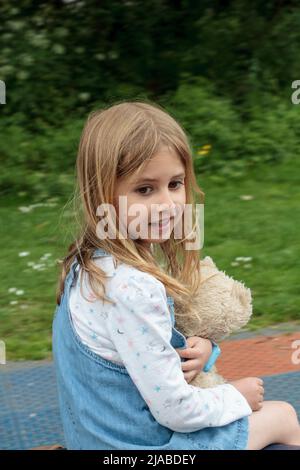 Une fille de 5 ans joue dans le parc tout en tenant son ours en peluche Banque D'Images