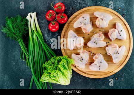 Les ailes de poulet crues reposent sur un support rond sur un fond noir aux épices. Banque D'Images