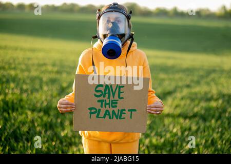 Personne dans le masque à gaz tient le carton avec un appel à sauver la planète Banque D'Images