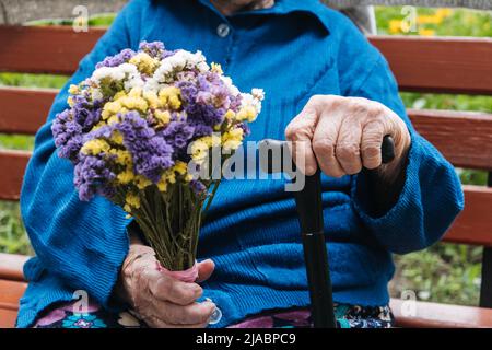 Soutien aux personnes âgées. Associations caritatives pour personnes âgées. Gros plan des mains de femme âgée avec bouquet de fleurs. Banque D'Images