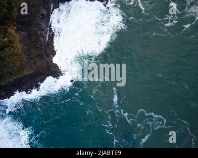 Vue aérienne. Un océan turquoise aux vagues de lumière blanche bat contre une côte rugueuse, inégale, recouverte de mousse. Paysages marins pittoresques, scènes calmes. Confortable et romantique Banque D'Images