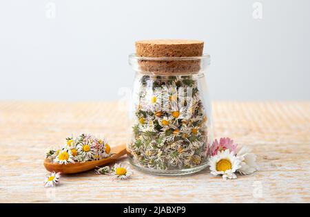 Plante médicinale à base de plantes séchées, la pâquerette commune, également connue sous le nom de Bellis Perennis. Fleurs sèches dans un pot en verre et une cuillère en bois, prêtes pour faire du thé à base de plantes Banque D'Images